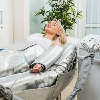 Blonde girl lying with closed eyes during pressotherapy session in clinic